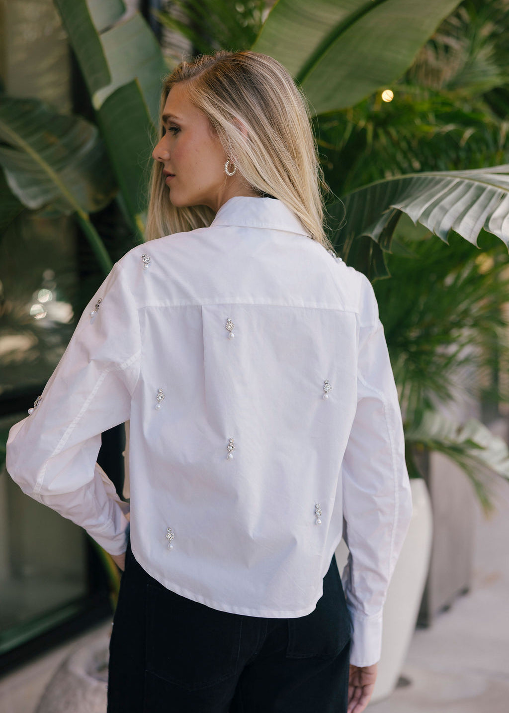 Woman wearing a white blouse with floral embellishments in an outdoor setting.