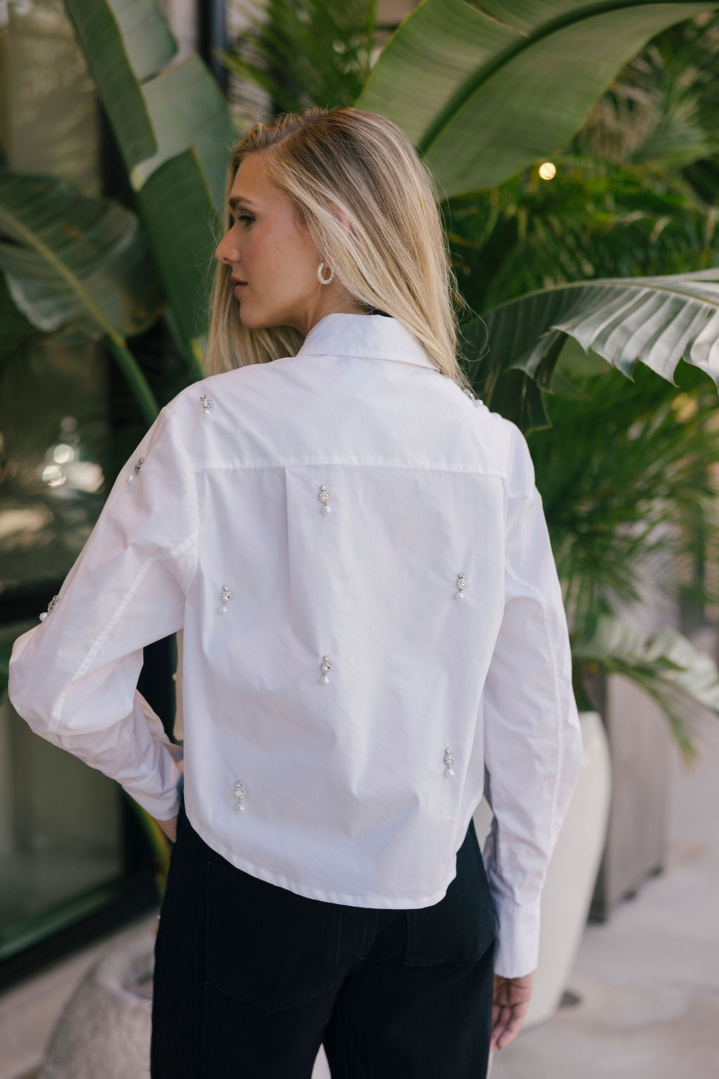 Woman wearing a white blouse with floral embellishments in an outdoor setting.