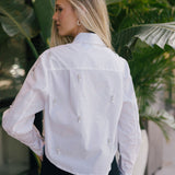 Woman wearing a white blouse with floral embellishments in an outdoor setting.
