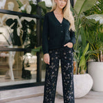 Woman wearing a dark outfit with floral patterns standing in front of a store window.