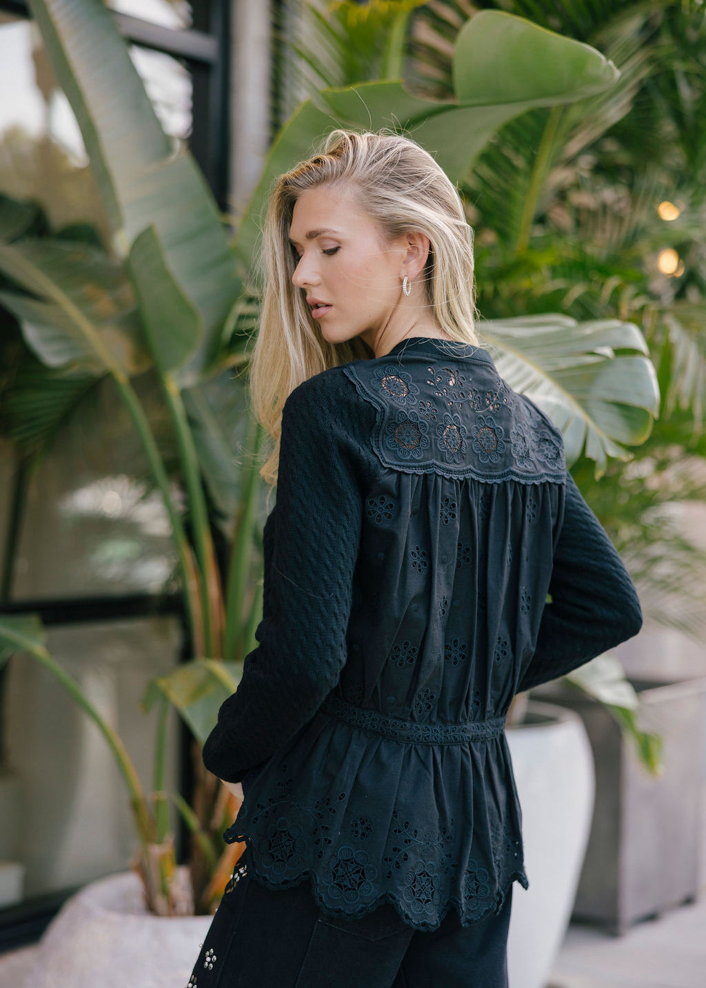 Woman wearing a black embroidered jacket in an outdoor setting with plants.