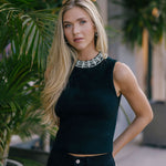 Woman wearing a Black sleeveless top with embellishments, standing among plants.