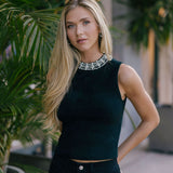 Woman wearing a Black sleeveless top with embellishments, standing among plants.