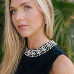Woman wearing a black sleeveless top with crystals on the collar against a blurred natural background