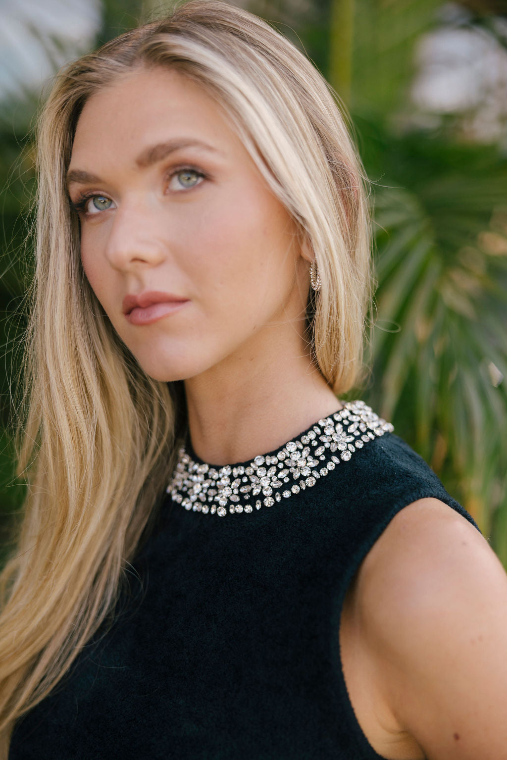 Woman wearing a black sleeveless top with crystals on the collar against a blurred natural background