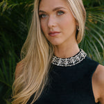 Woman wearing a black top with beading on the collar against a green leafy background