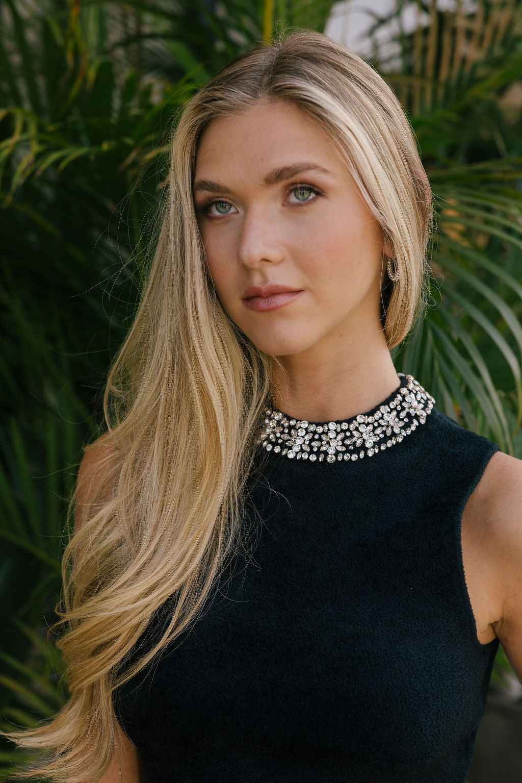 Woman wearing a black top with beading on the collar against a green leafy background