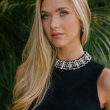 Woman wearing a black top with beading on the collar against a green leafy background