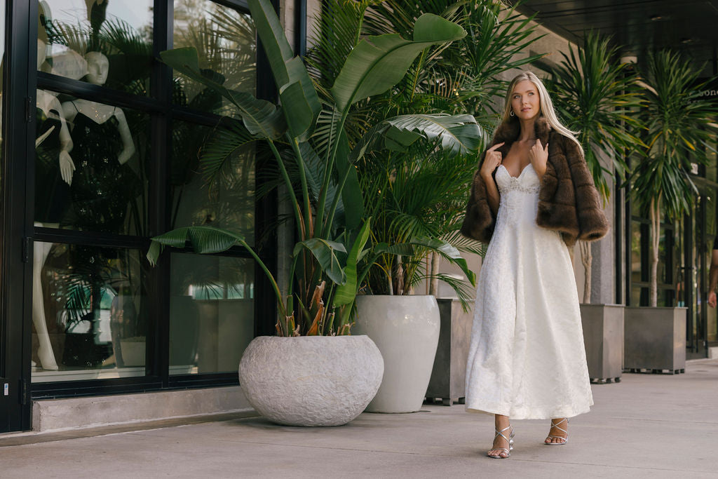 Woman in a white dress standing among potted plants in an indoor setting