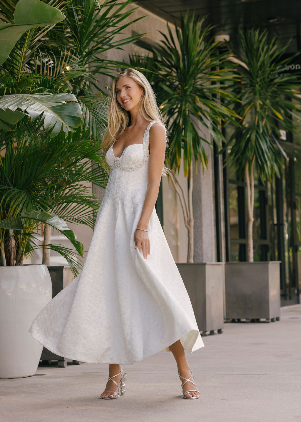 Woman in a white dress standing outdoors with greenery in the background