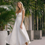 Woman in a white dress standing outdoors with greenery in the background