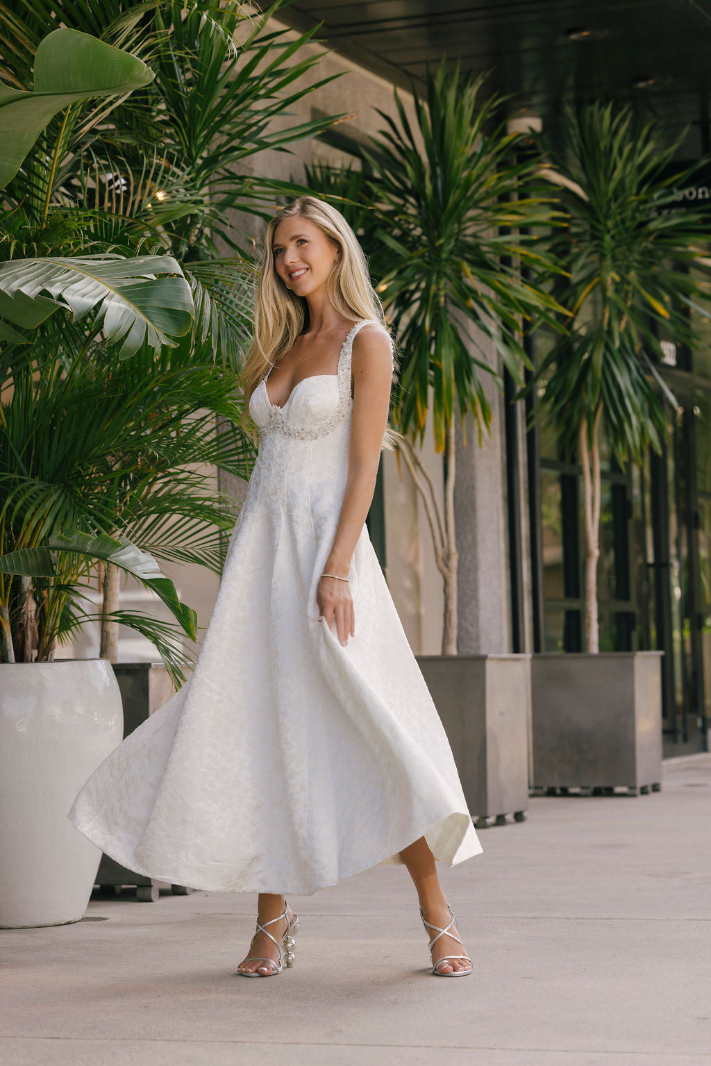 Woman in a white dress standing outdoors with greenery in the background
