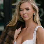 Woman in a white lace dress holding a brown fur coat with a blurred background