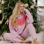 Woman in a pink tracksuit sitting in front of a decorated Christmas tree.