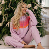 Woman in a pink tracksuit sitting in front of a decorated Christmas tree.