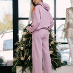 Woman in a mauve tracksuit standing in front of a decorated Christmas tree.