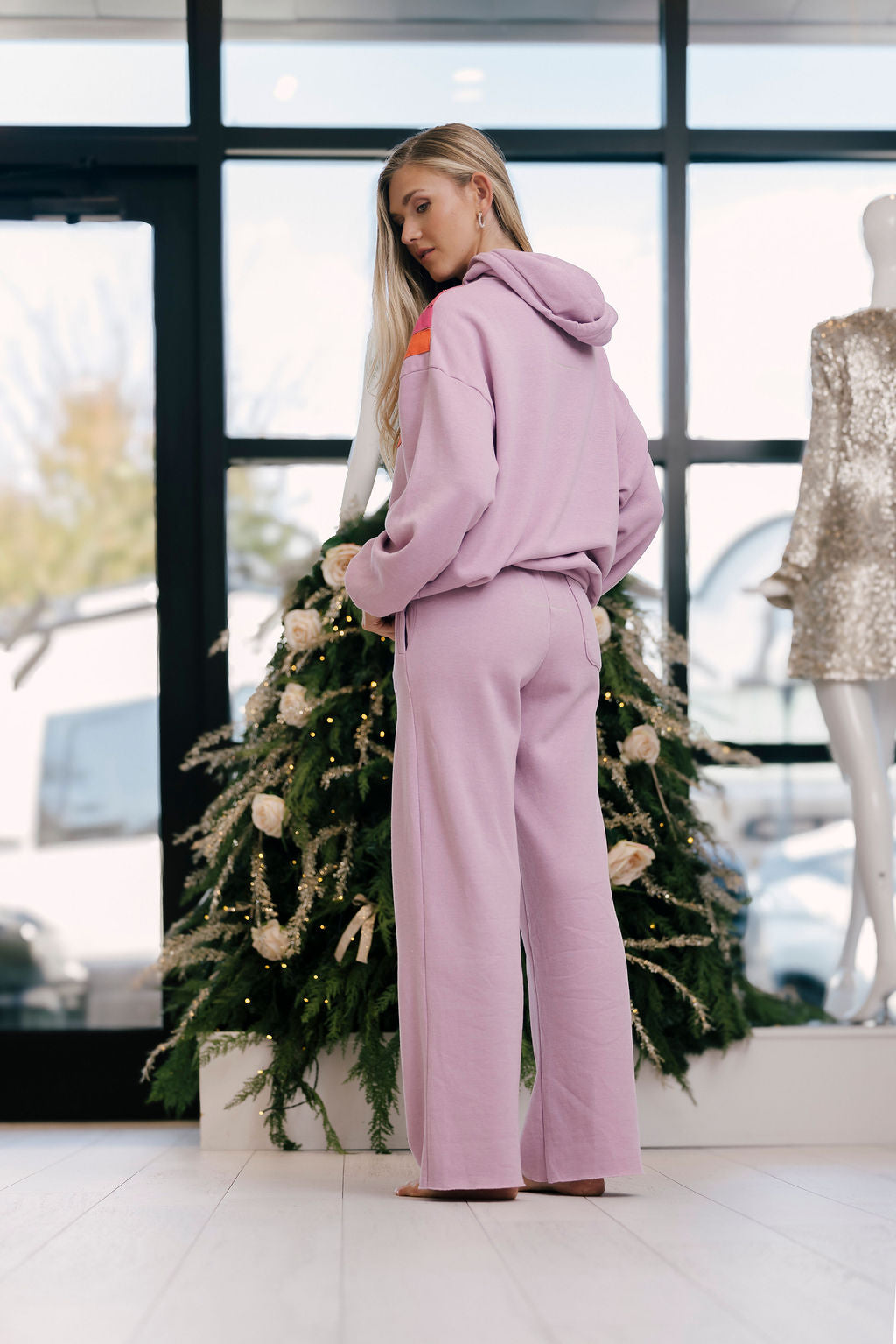 Woman in a mauve tracksuit standing in front of a decorated Christmas tree.