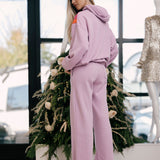 Woman in a mauve tracksuit standing in front of a decorated Christmas tree.