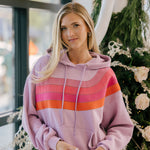 Woman wearing a pink striped hoodie holding a cupcake in front of a decorated Christmas tree.