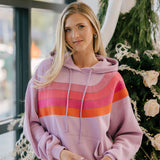 Woman wearing a pink striped hoodie holding a cupcake in front of a decorated Christmas tree.