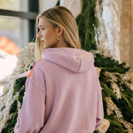 Woman wearing a mauve hoodie standing in front of a decorated Christmas tree.