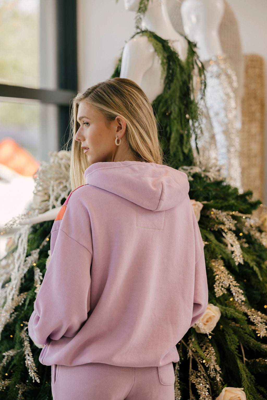 Woman wearing a mauve hoodie standing in front of a decorated Christmas tree.