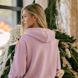 Woman wearing a mauve hoodie standing in front of a decorated Christmas tree.