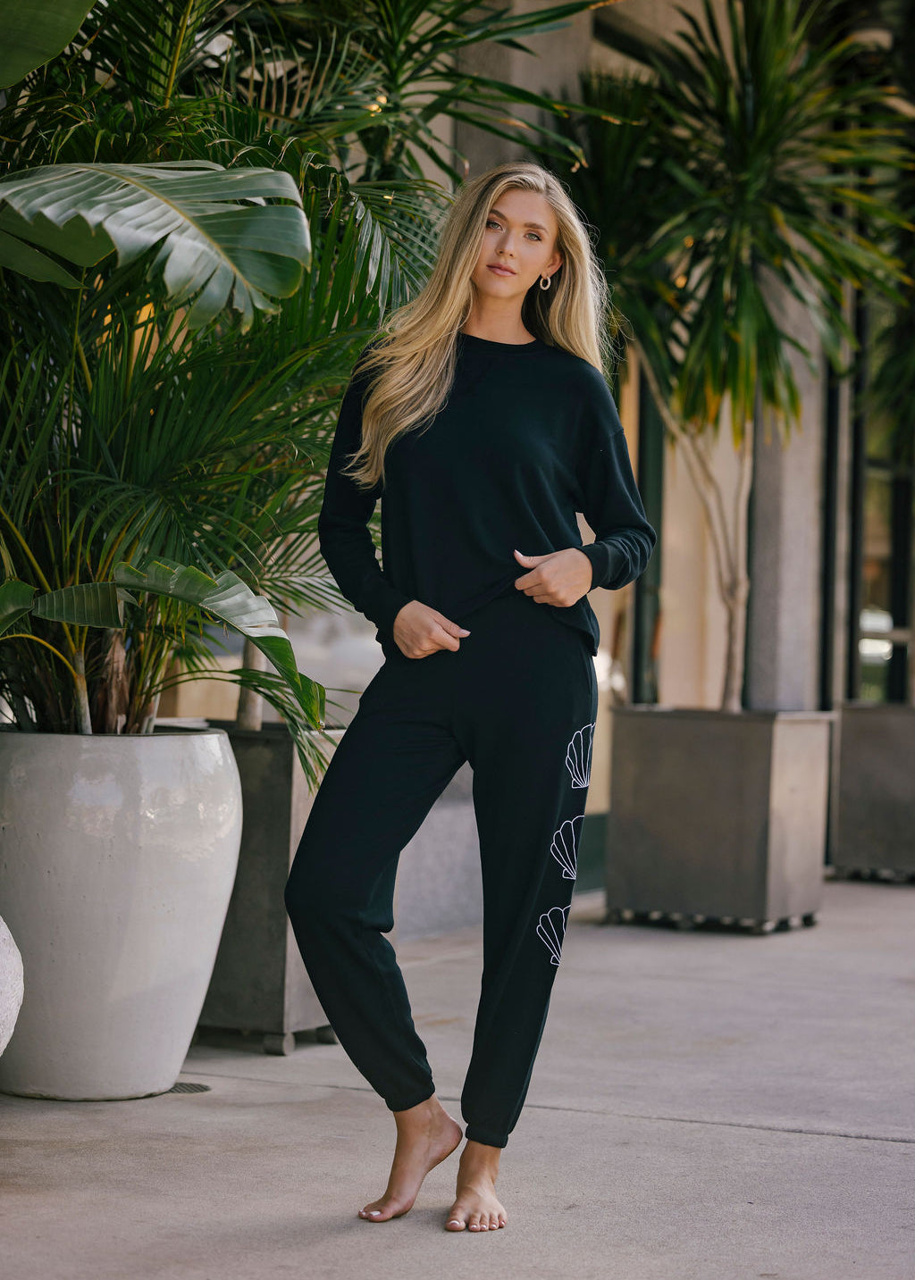 Woman in black outfit standing outdoors with plants in the background