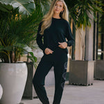 Woman in black outfit standing outdoors with plants in the background