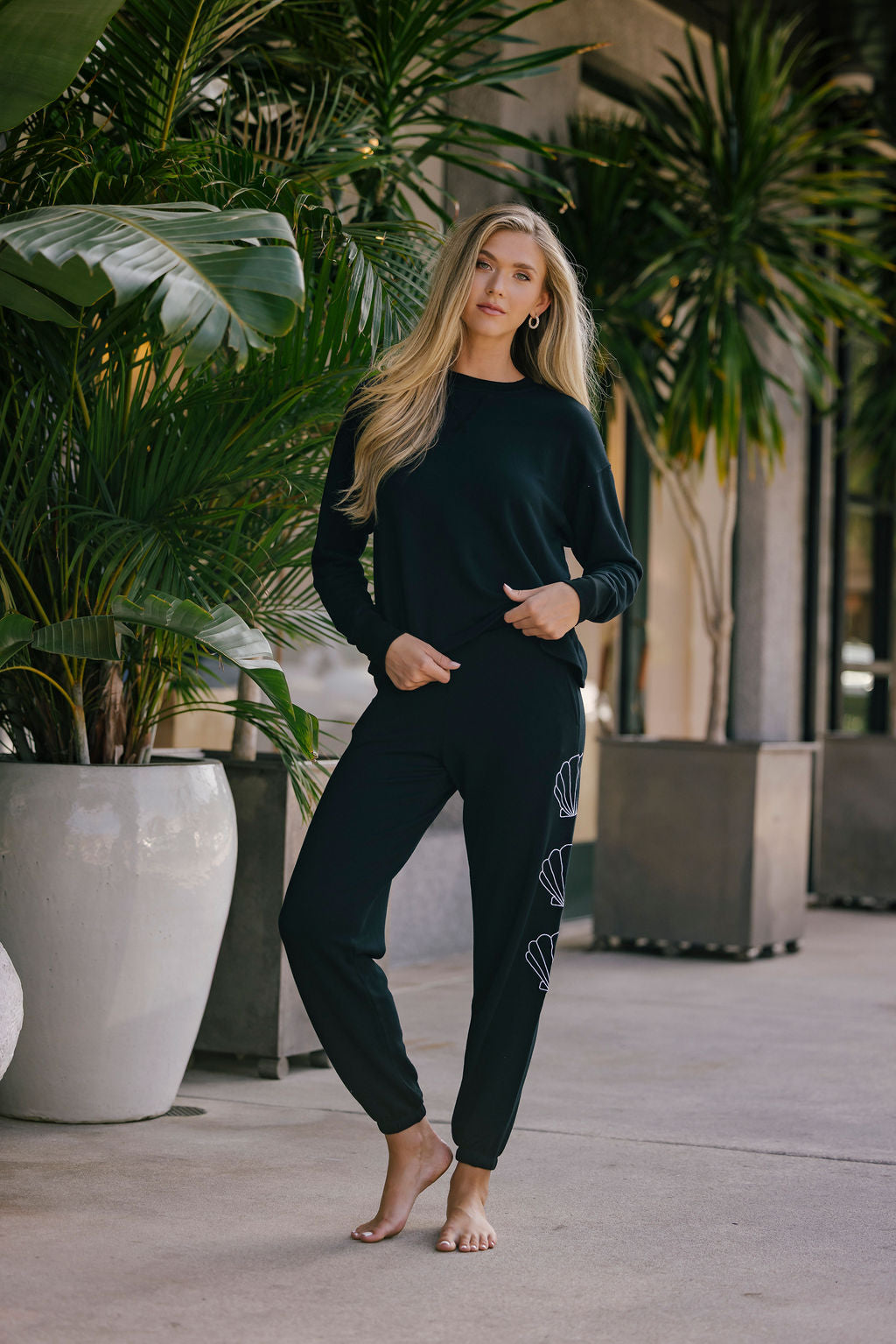 Woman in black outfit standing outdoors with plants in the background