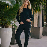 Woman in black outfit standing outdoors with plants in the background