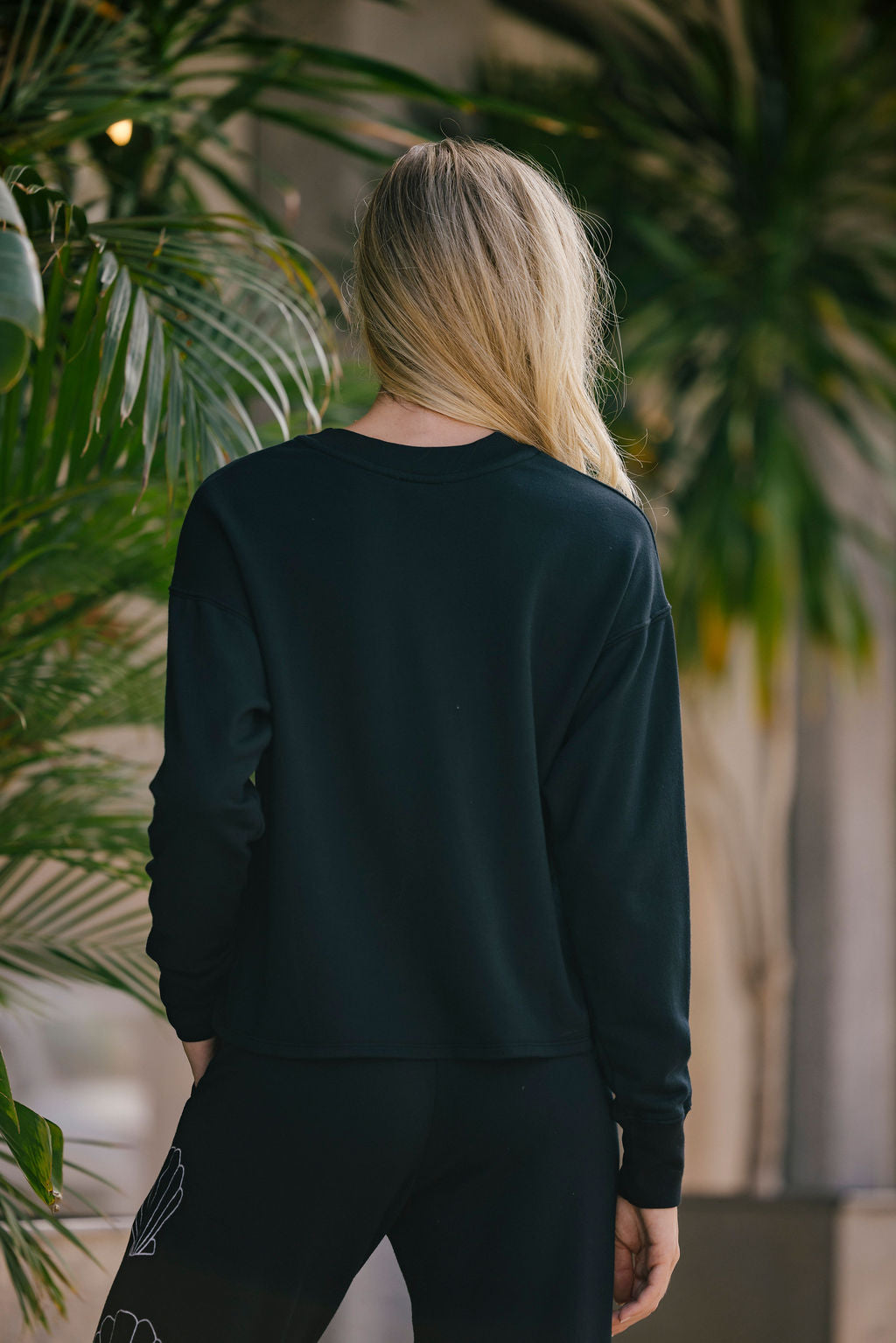 Person wearing a black sweatshirt and pants standing in front of green plants