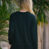 Person wearing a black sweatshirt and pants standing in front of green plants