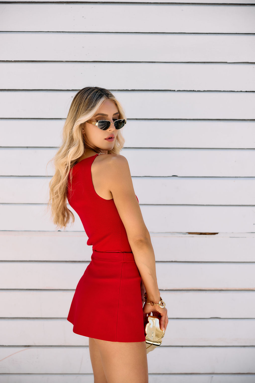 Woman in a red outfit with gold accessories standing against a white wooden background