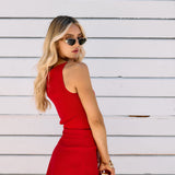 Woman in a red outfit with gold accessories standing against a white wooden background