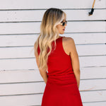 Woman wearing a red top and skort standing against a white wooden wall.
