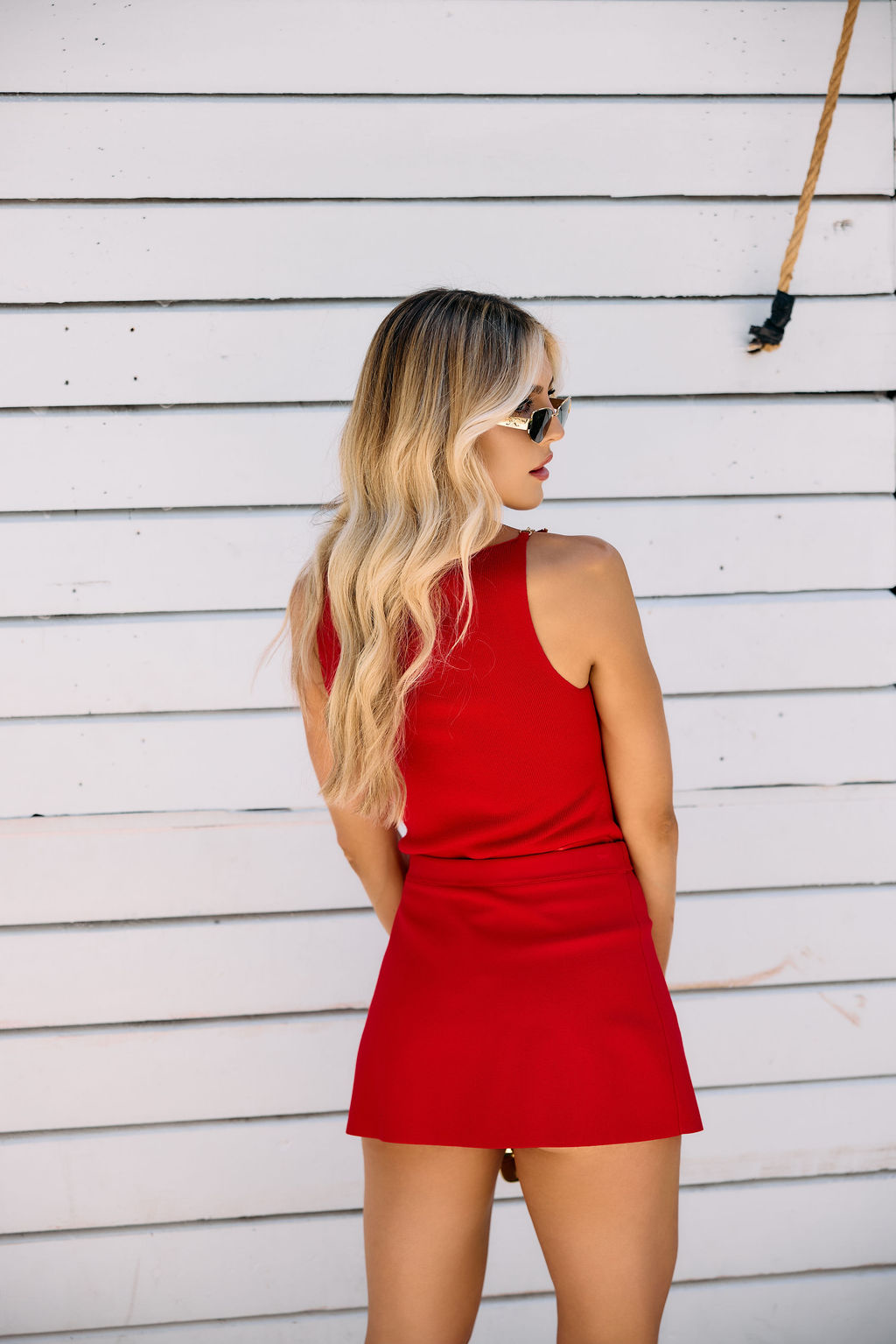 Woman wearing a red top and skort standing against a white wooden wall.