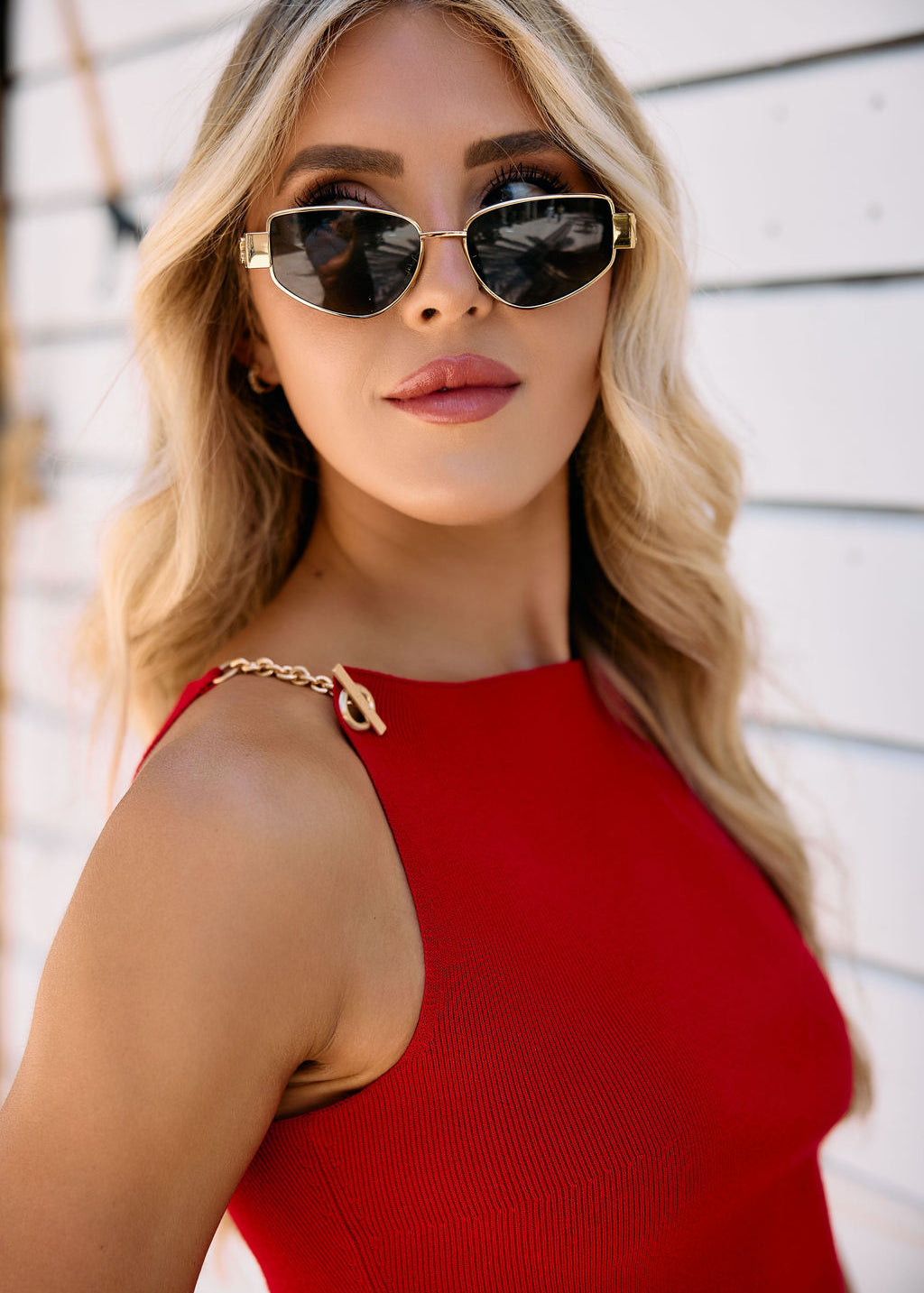 Woman wearing sunglasses and a red top with chain detailing against a white background