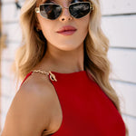Woman wearing sunglasses and a red top with chain detailing against a white background