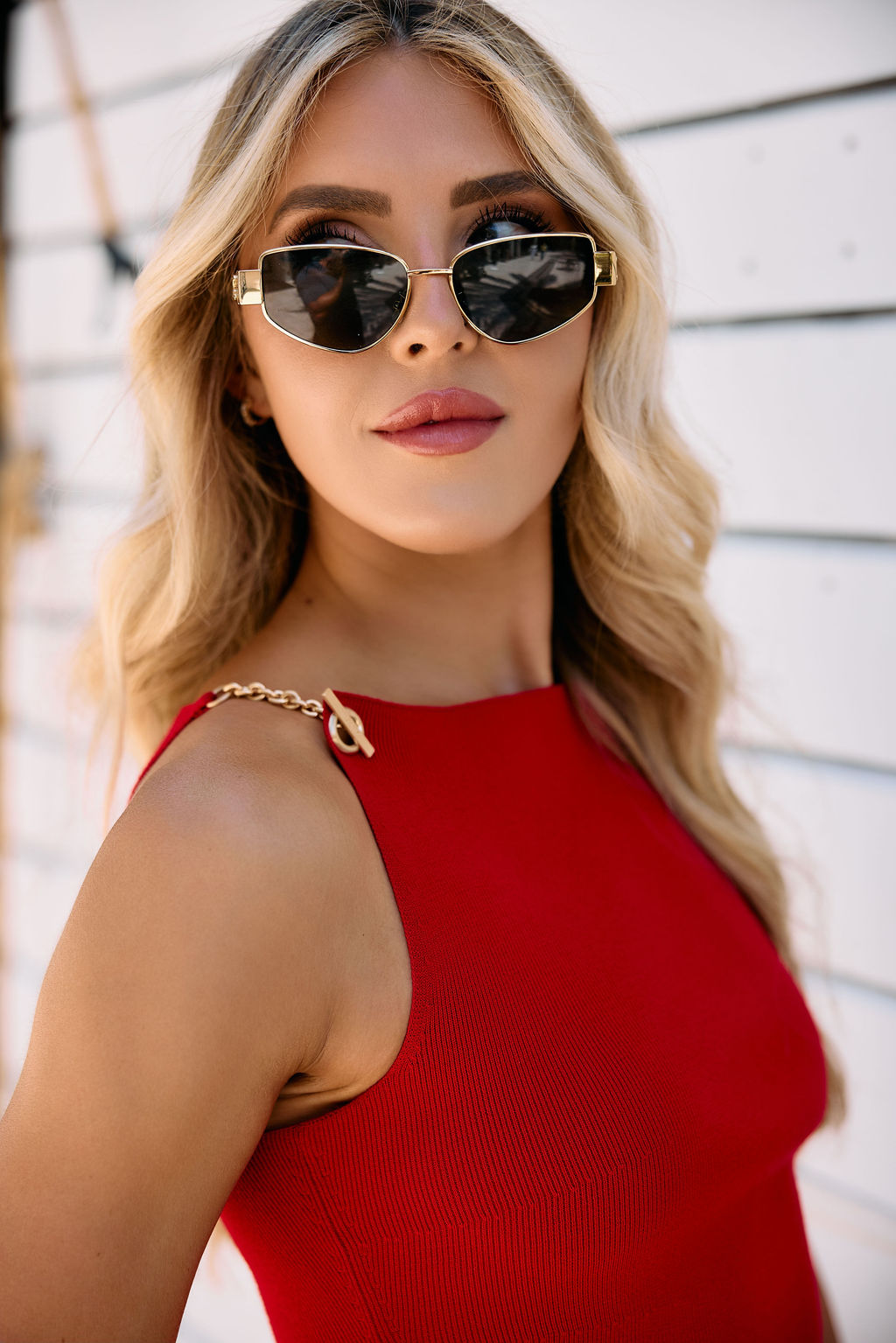 Woman wearing sunglasses and a red top with chain detailing against a white background