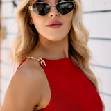 Woman wearing sunglasses and a red top with chain detailing against a white background