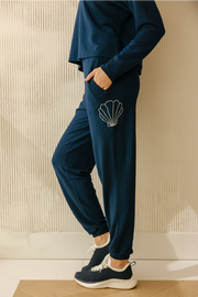 A person wearing navy blue soft shell joggers with a contrasting white shell embroidery at the hip, standing with hands in pockets.