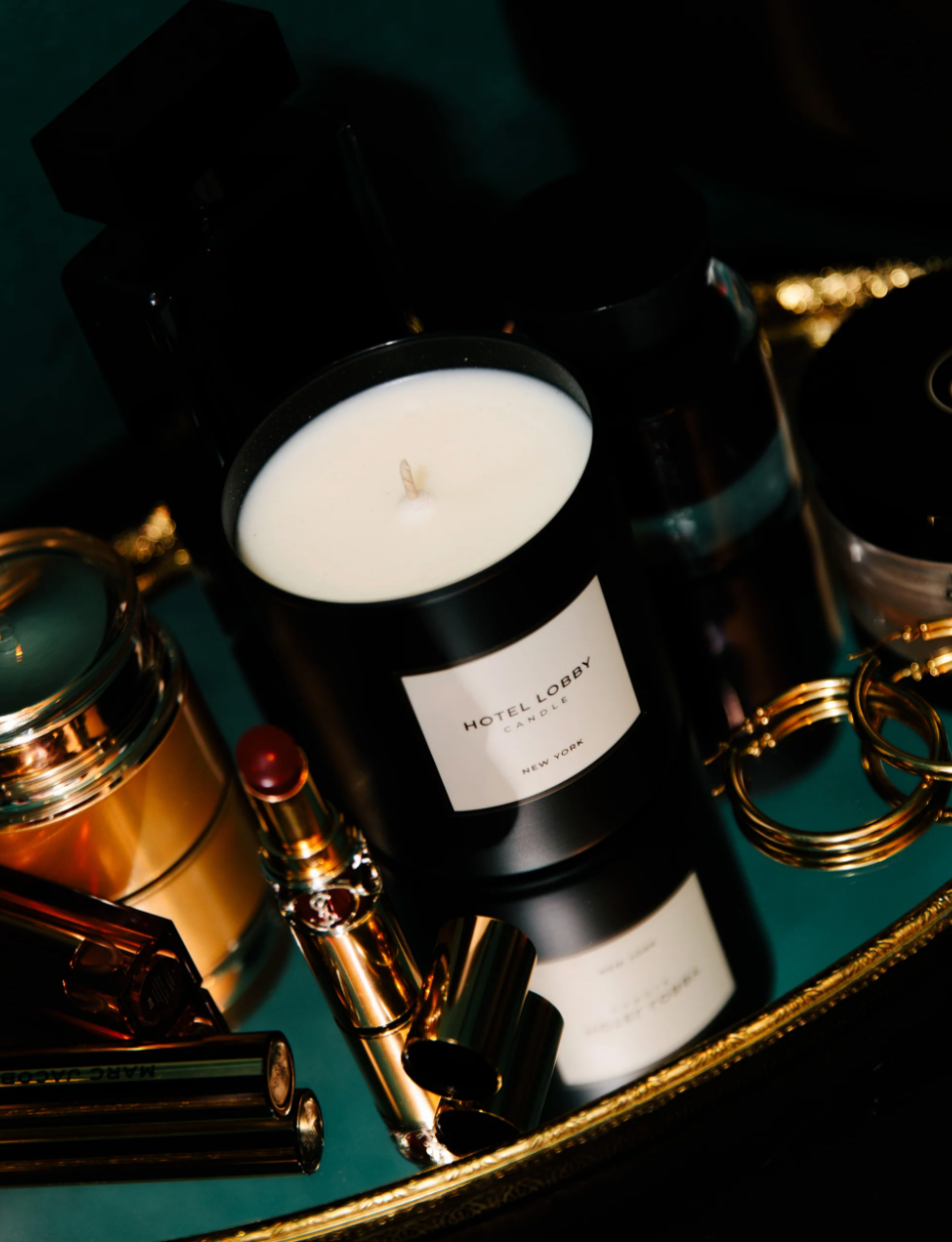 Candle in a black container with a label on a reflective surface, surrounded by decorative items.