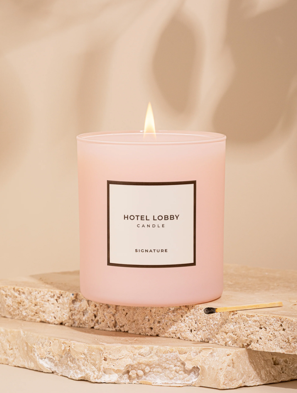 Pink candle labeled 'Hotel Lobby' on a beige stone surface with a soft background