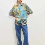 Person wearing a floral blouse and blue jeans with embroidery on a plain background