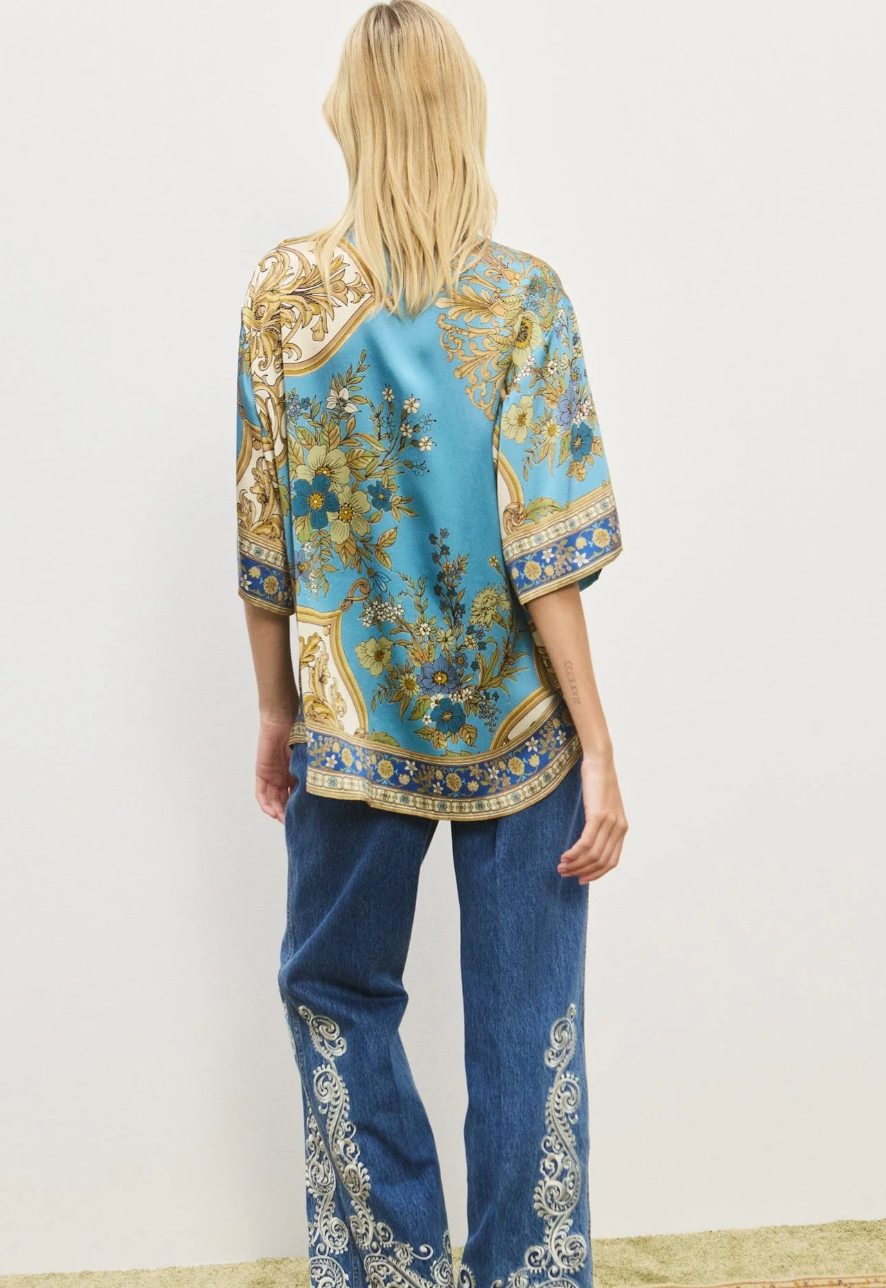 Woman wearing a patterned top and jeans on a white background
