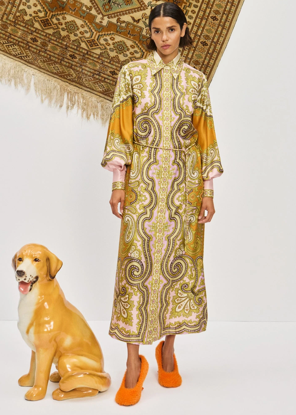 Woman in a patterned dress standing next to a dog statue on a white background
