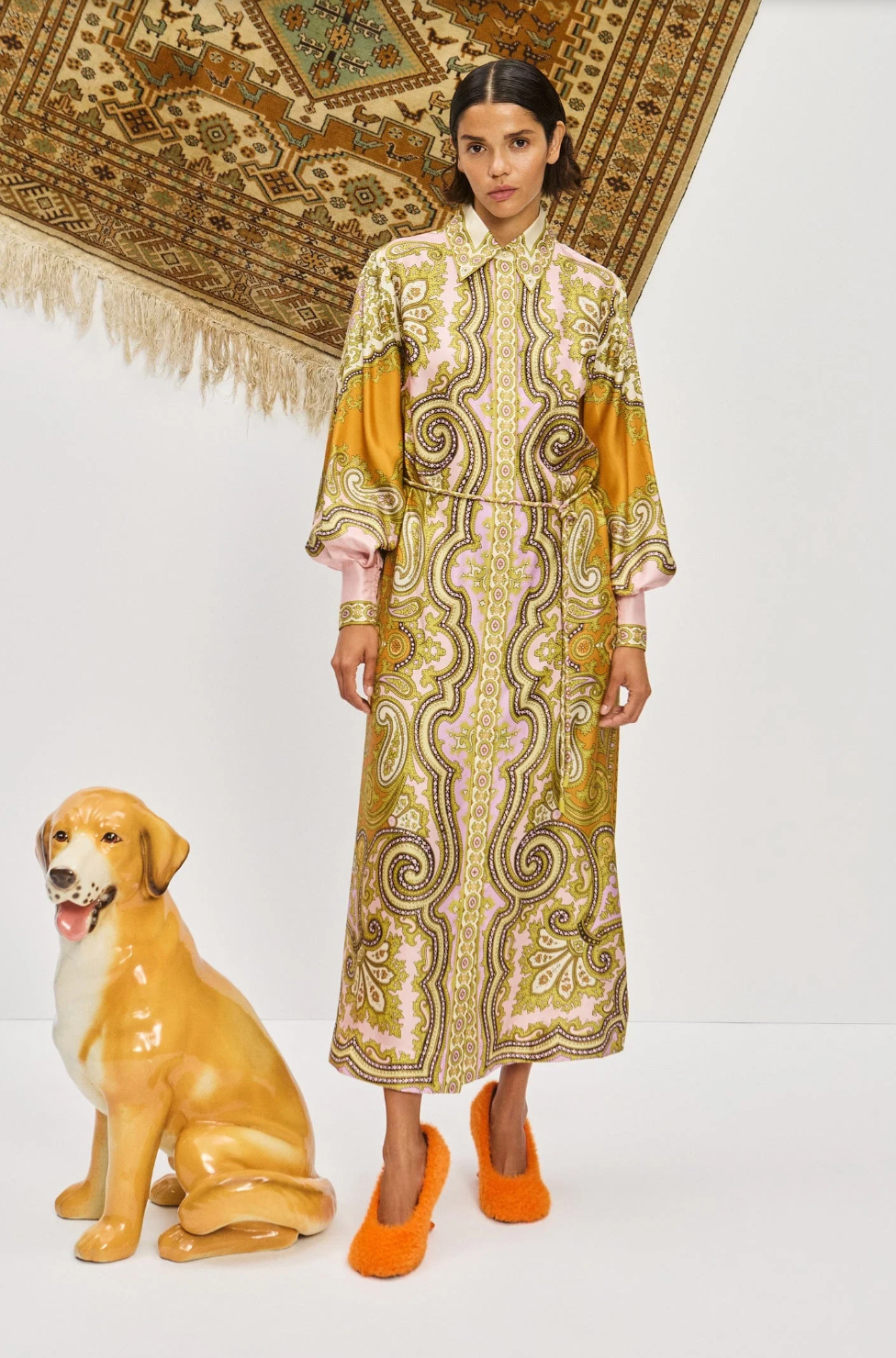 Woman in a patterned dress standing next to a dog statue on a white background