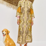 Woman in a patterned dress standing next to a dog statue on a white background