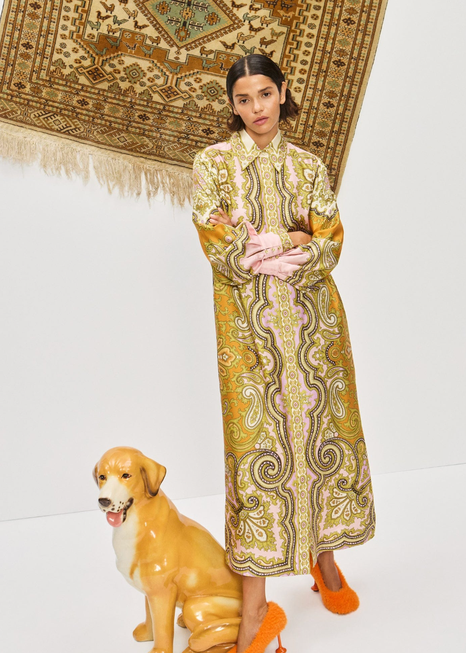 Woman in a patterned dress standing next to a ceramic dog on a white background